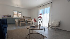 A modern living room with a dining area, a sofa, a coffee table, and a view of the outside.