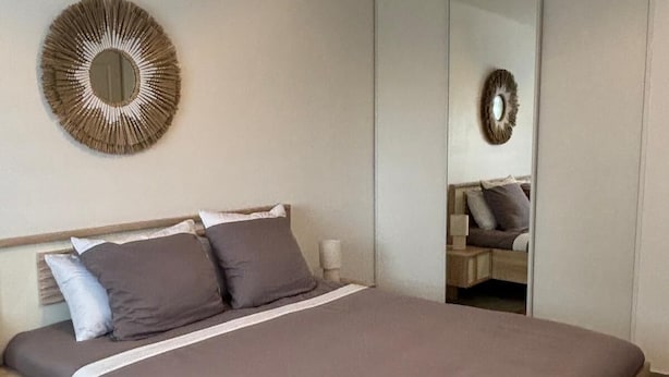 A modern bedroom with a wooden bed, a round mirror, and a unique ceiling light fixture.
