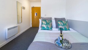 A hotel room with a bed, a nightstand, a mirror, a door, and a radiator. - The Croft (Derby)