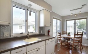 A modern kitchen with white cabinets, a built-in dishwasher, and a dining area with wooden chairs and a table. - Charming 3-bedroom townhome with WiFi, AC in Seaside Heights (Seaside Heights)