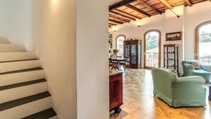 A spacious living area with a wooden floor, a staircase, and a dining area visible through an arched doorway. - Authentic Roman Escape with Private Terrace & City views (Roma)
