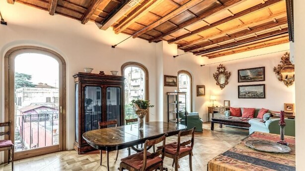 A spacious room with a wooden dining table, chairs, a sofa, and a patterned ottoman. - Authentic Roman Escape with Private Terrace & City views (Roma)