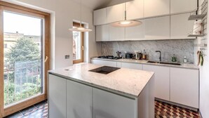 A modern kitchen with a large island, white cabinets, and a view of the outdoors through a large window. - Authentic Roman Escape with Private Terrace & City views (Roma)