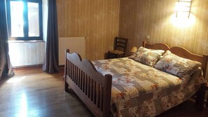 Ein Schlafzimmer mit einem hölzernen Bett, einem Sessel, einem Fenster mit Vorhängen und einer Wandleuchte.