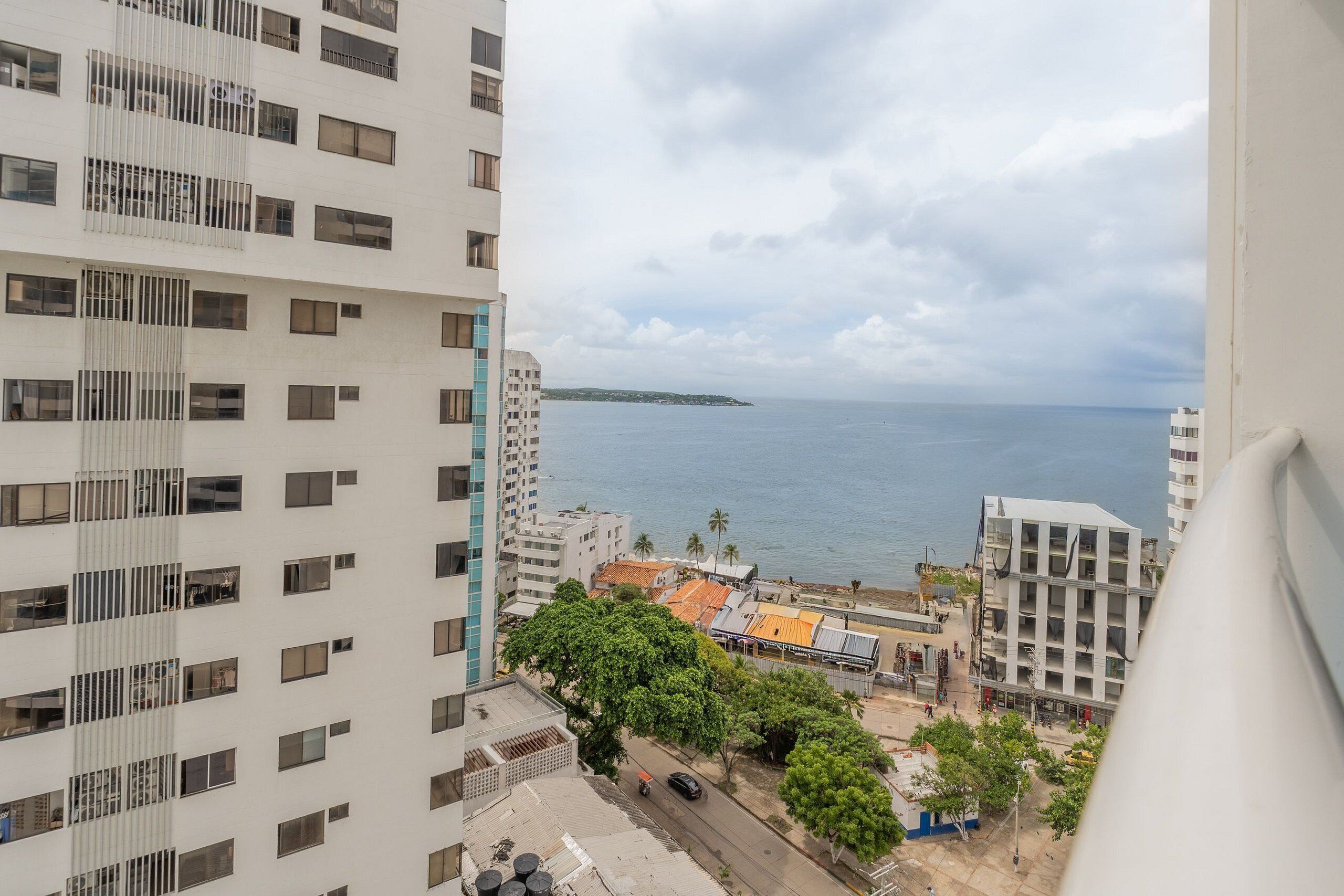 Ein Hochhaus mit mehreren Stockwerken, Blick auf das Meer und eine kleine baumbestandene Fläche im Vordergrund.