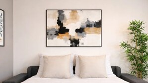 A hotel room with a bed, two pillows, a framed abstract painting, a green plant, and two towels with a bottle on them. - VIERGE (Paris)