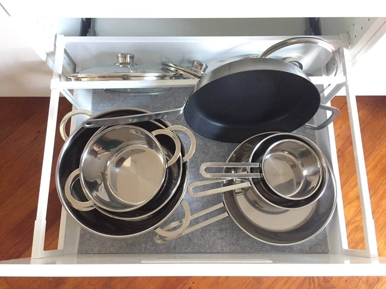 A kitchen drawer with stainless steel cookware including pots, pans, and lids.