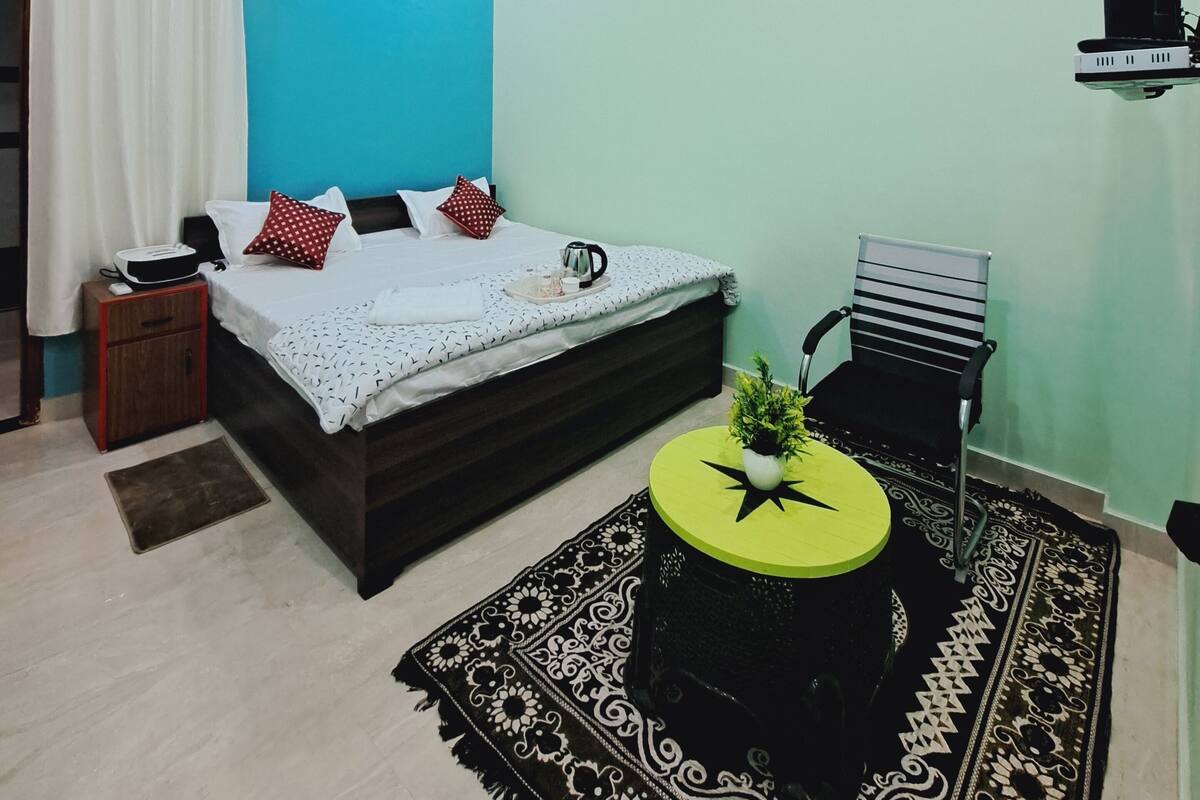 Quarto com cama, mesa de cabeceira, cadeira e um objeto decorativo na parede.