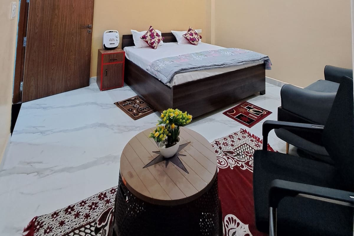 Quarto com cama, escrivaninha, cadeira, ventilador de teto e televisão fixada na parede.