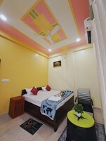 A bedroom with a bed, a nightstand, a small table with a plant, a ceiling fan, and an air conditioning unit.