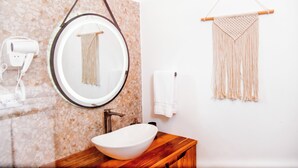 A bathroom with a round mirror, a white sink, a towel rack, and a macrame wall hanging. - Central Hotel Boutique (Las Galeras)
