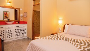 A hotel room with a bed, a bedside table, a nightstand, a mirror, a sink, and a towel rack. - Central Hotel Boutique (Las Galeras)