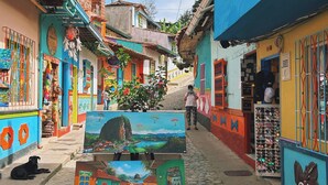A narrow cobblestone street with colorful buildings, a street lamp, and a painting on display. - Suites del Lago (Marinilla)