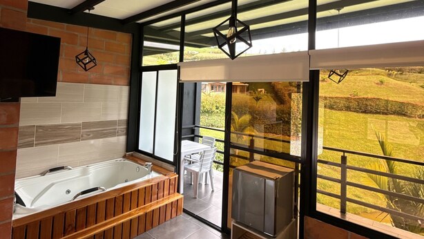 A modern bathroom with a bathtub, a wooden bench, and a large window offering a view of a garden. - Suites del Lago (Marinilla)