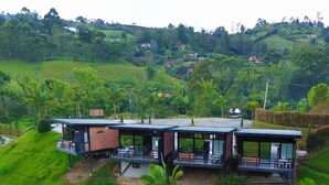 A modern house with a flat roof, large windows, and a balcony, surrounded by lush greenery and a pond. - Suites del Lago (Marinilla)
