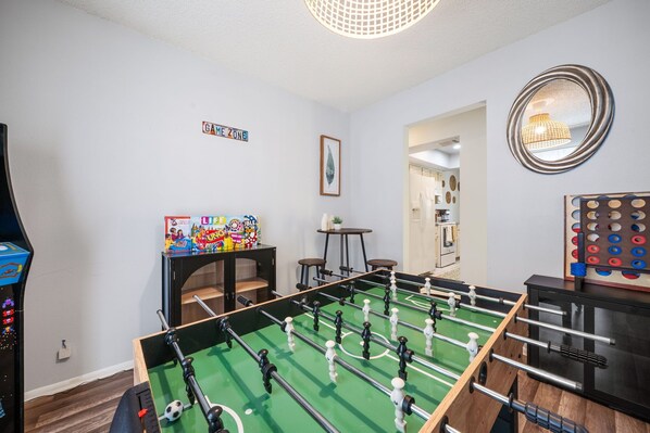 Une pièce comprenant un baby-foot, un meuble pour baby-foot, une petite table avec une plante et un miroir au mur.