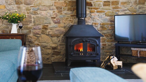 Et stue med stenvægge, en brændeovn, et fjernsyn og et glas vin på et bord.