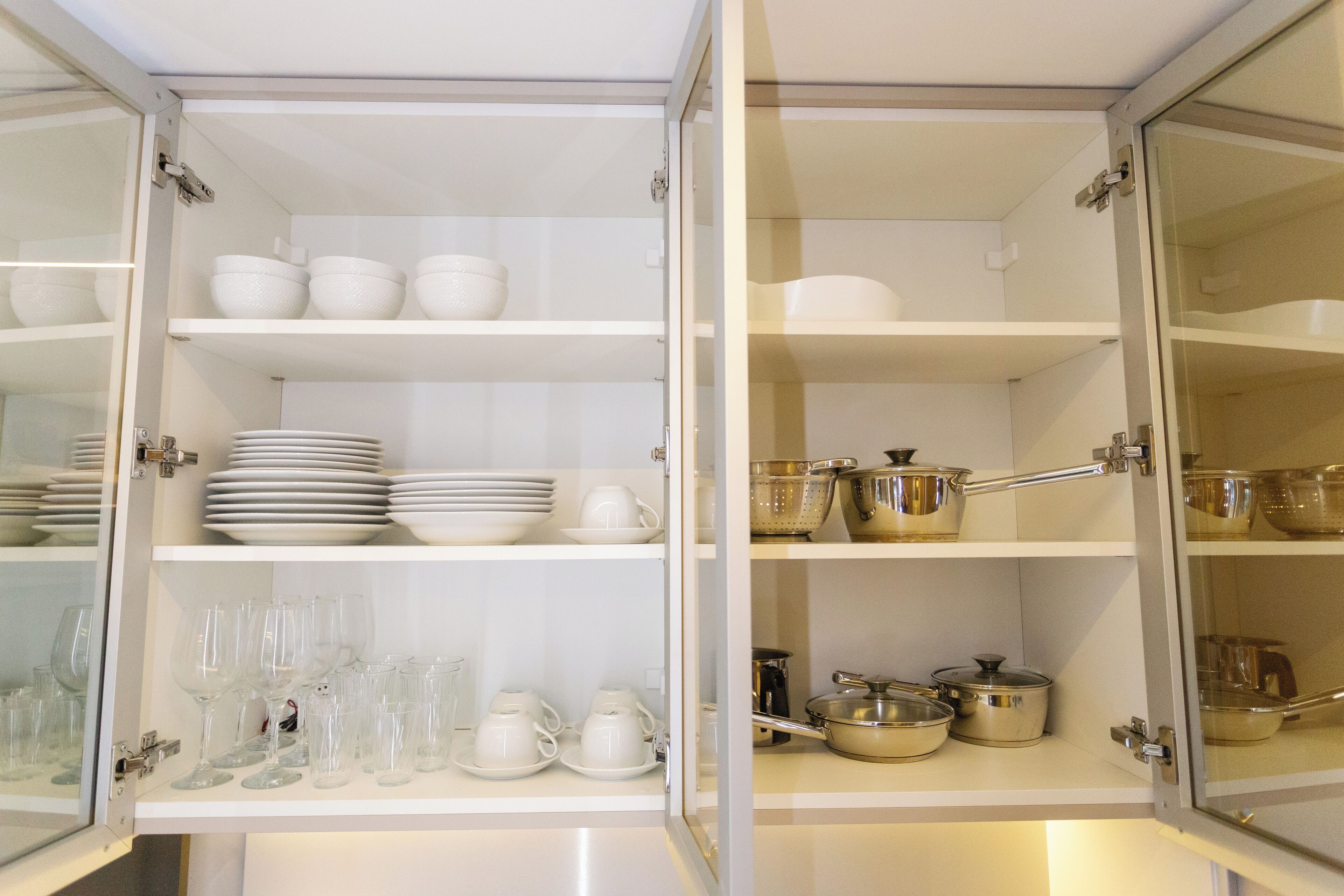 Un mueble de cocina con estantes que contienen cuencos, platos y cristalería blancos.