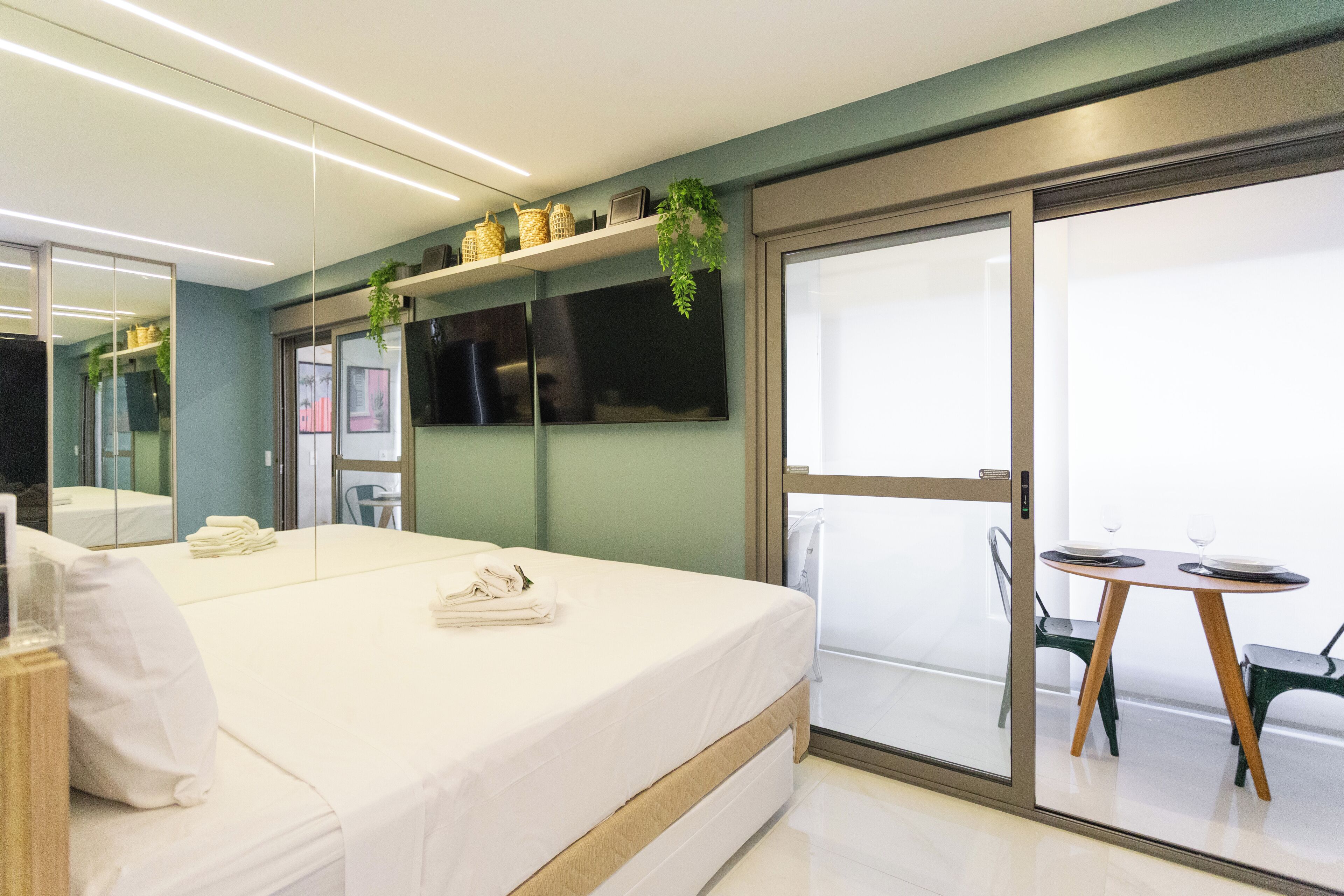 A modern hotel room with a large bed, a glass door leading to a balcony, and a small table with chairs.