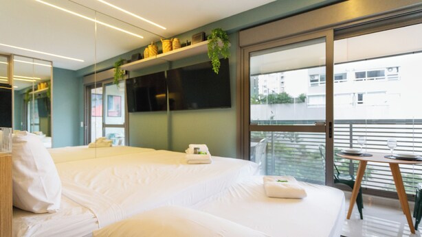 A modern hotel room with a large bed, a small table, and a balcony with a view of the city. - Haus Mitre Alto Butantã (Sao Paulo)