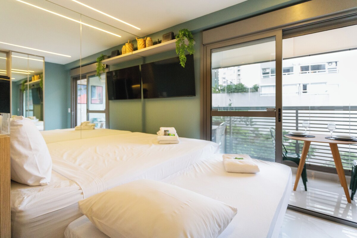 A modern hotel room with a large bed, a small table, and a balcony with a view of the city.