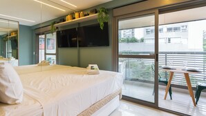 A modern hotel room with a large bed, a balcony with a table and chairs, and a view of the cityscape. - Haus Mitre Alto Butantã (Sao Paulo)