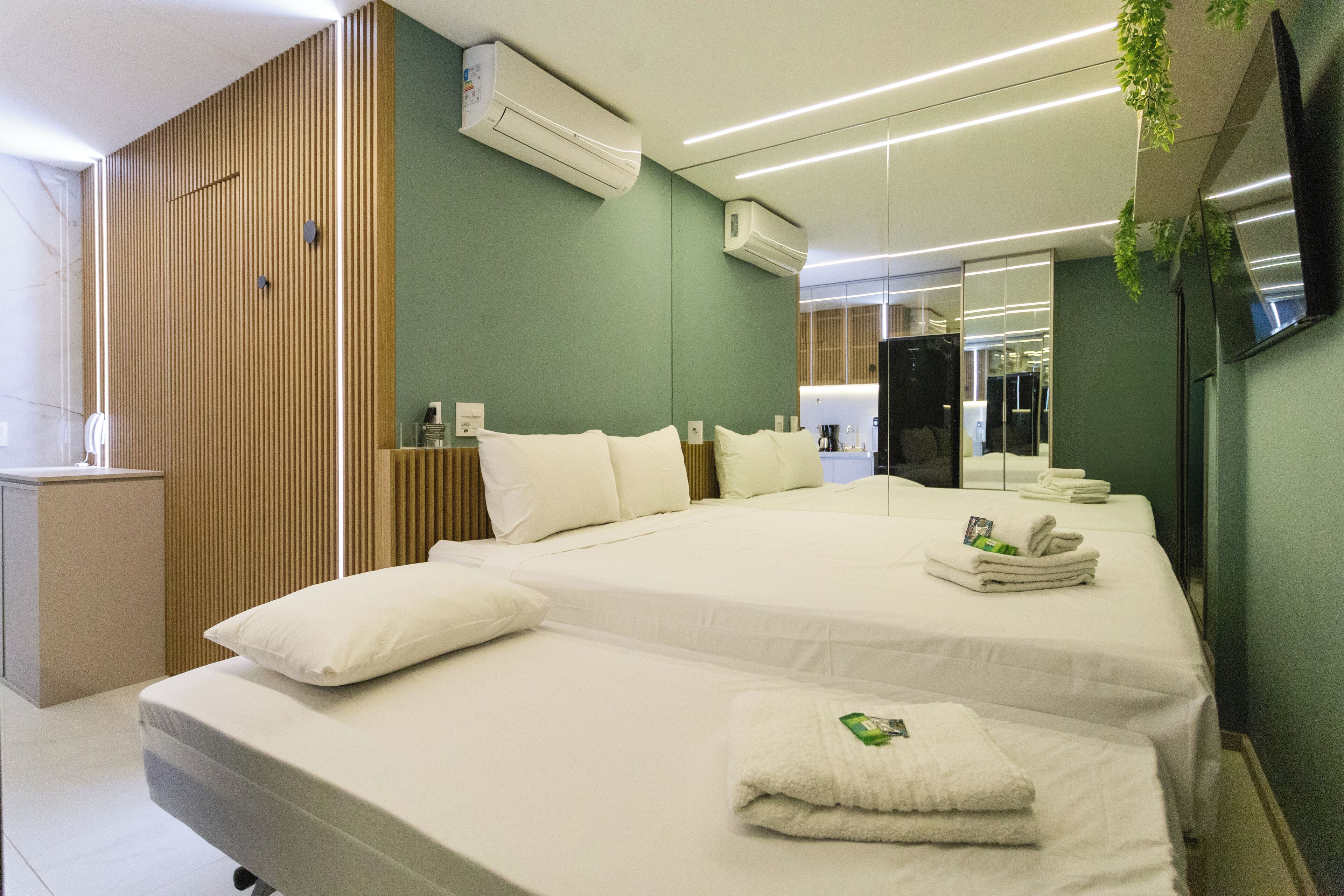 Una habitación de hotel moderna con dos camas, un panel de pared de madera, un equipo de aire acondicionado y un televisor de pantalla plana.