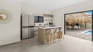 A modern kitchen with a central island, stainless steel appliances, and a dining area with a thatched roof outside. - Elisabeth Resort Villa 37 with Private Pool at Mambo Beach Boulevard (Willemstad)