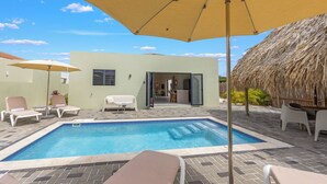 A swimming pool with lounge chairs and umbrellas, a thatched roof structure, and a building with a sliding door. - Elisabeth Resort Villa 37 with Private Pool at Mambo Beach Boulevard (Willemstad)