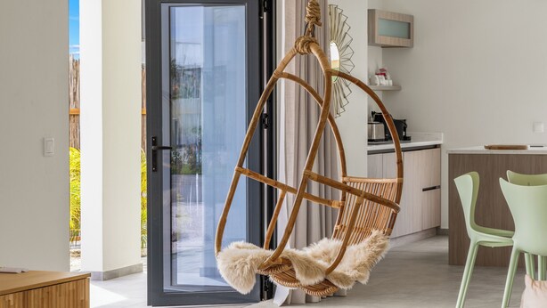 A modern living room with a wicker hanging chair, a green chair, and a kitchen area in the background. - Elisabeth Resort Villa 37 with Private Pool at Mambo Beach Boulevard (Willemstad)