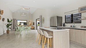 A modern kitchen with a central island, bar stools, and a dining area with a green table and chairs. - Elisabeth Resort Villa 37 with Private Pool at Mambo Beach Boulevard (Willemstad)