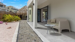 A modern outdoor patio area with a seating arrangement, a thatched-roof structure, and a pathway leading to a building entrance. - Elisabeth Resort Villa 37 with Private Pool at Mambo Beach Boulevard (Willemstad)
