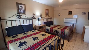 A room with two beds, each with a patterned bedspread, a small bedside table, a wall-mounted lamp, and a ceiling fan. - John Wayne Suite (Buchanan Dam)