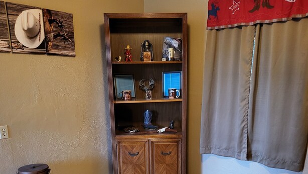 A corner room with a wooden cabinet, a small stool, and a window with curtains. - John Wayne Suite (Buchanan Dam)