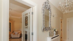 Un couloir avec une console blanche, un grand miroir décoratif et un lustre.