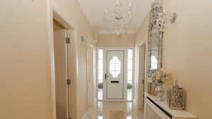 Un couloir avec une porte blanche, un lustre et une console ornée d’objets décoratifs.