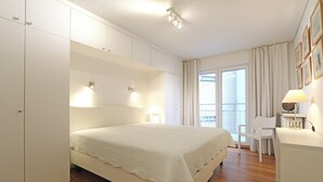 Un dormitorio con una cama grande, un armario blanco y un escritorio con una lámpara.