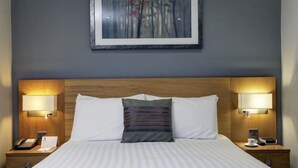 Ein Hotelzimmer mit einem großen Bett, zwei Nachttischlampen, einem Telefon, einer Tasse und einem gerahmten Bild an der Wand.
