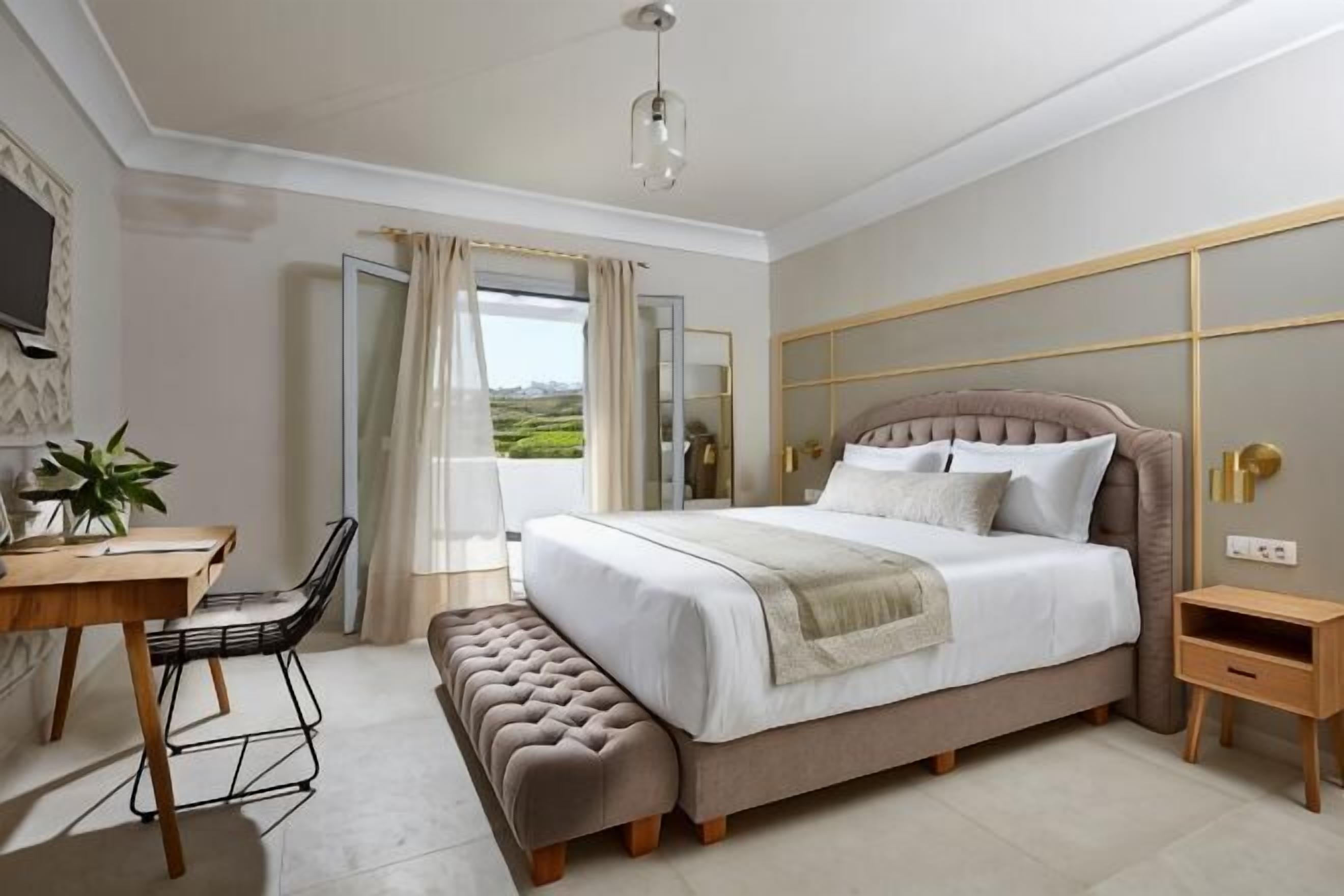 A bedroom with a bed, bedside table, chair, desk, and a view of the outdoors.