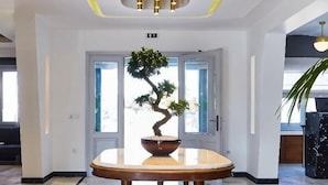 Un hall d’entrée agrémenté d’un bonsaï posé sur une table ronde, d’un lustre moderne et d’une porte à panneaux de verre.