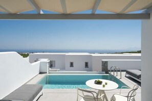 A rooftop pool with a table and chairs, a view of the sea, and white buildings in the background. - De Sol Hotel & Spa (Santorini)