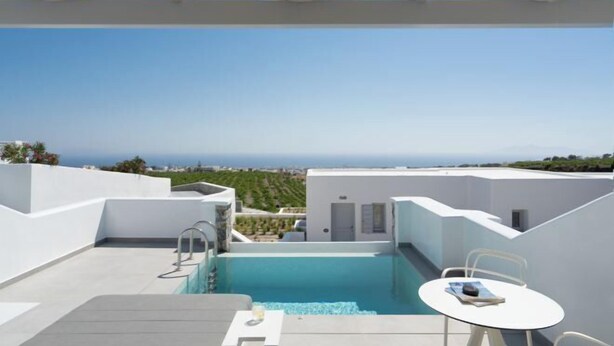 Une piscine sur le toit, agrémentée d’une table et de chaises, entourée de murs blancs et offrant une vue dégagée sur le paysage.