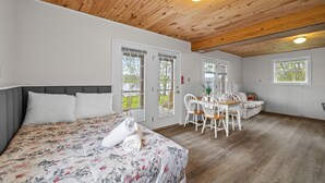 Ein Schlafzimmer mit einem Bett, einem Schreibtisch und einem Stuhl. Es gibt zwei Fenster und eine Tür.