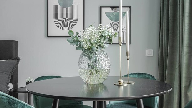 A round dining table with a glass vase of flowers, surrounded by green velvet chairs. - Modern Studios by Karolinska Institutet (Stockholm)