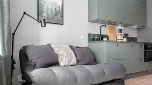 A modern living room with a grey sofa, a black floor lamp, and a kitchen area with grey cabinets and a green backsplash. - Modern Studios by Karolinska Institutet (Stockholm)