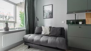 A modern bedroom with a grey sofa, a framed picture on the wall, and a window with curtains. - Modern Studios by Karolinska Institutet (Stockholm)