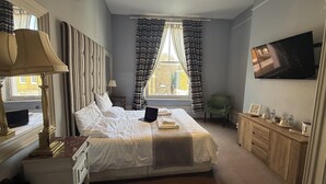 A hotel room with a large bed, a desk with a lamp, a television, and a view of the outside. - Crown and Sceptre (London)