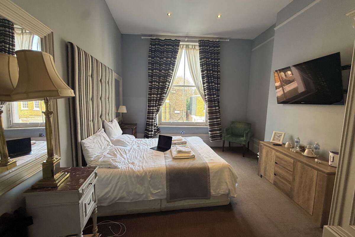 A hotel room with a large bed, a desk with a lamp, a television, and a view of the outside.