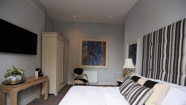 A bedroom with a large bed, a wooden desk, a chair, a television, and a painting on the wall. - Crown and Sceptre (London)