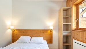 A bedroom with a wooden headboard, two bedside lamps, a white bed, and a built-in wooden wardrobe. - Apartment in Saint-sorlin Near Ski Slopes (Saint-Sorlin-d'Arves)